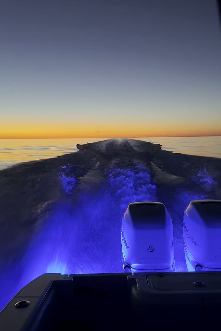 Running offshore out of Gulfport at dawn, wake lit blue behind twin Mercury outboards